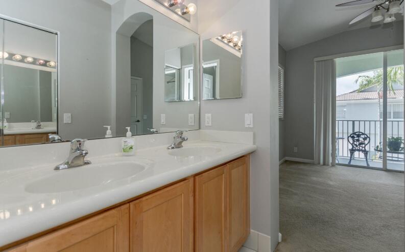 A bathroom with a double vanity and light wood cabinets leads to a carpeted room — 3019 Laurel Ridge Circle, Riviera Beach FL 33404, RIVIERA BEACH, FL