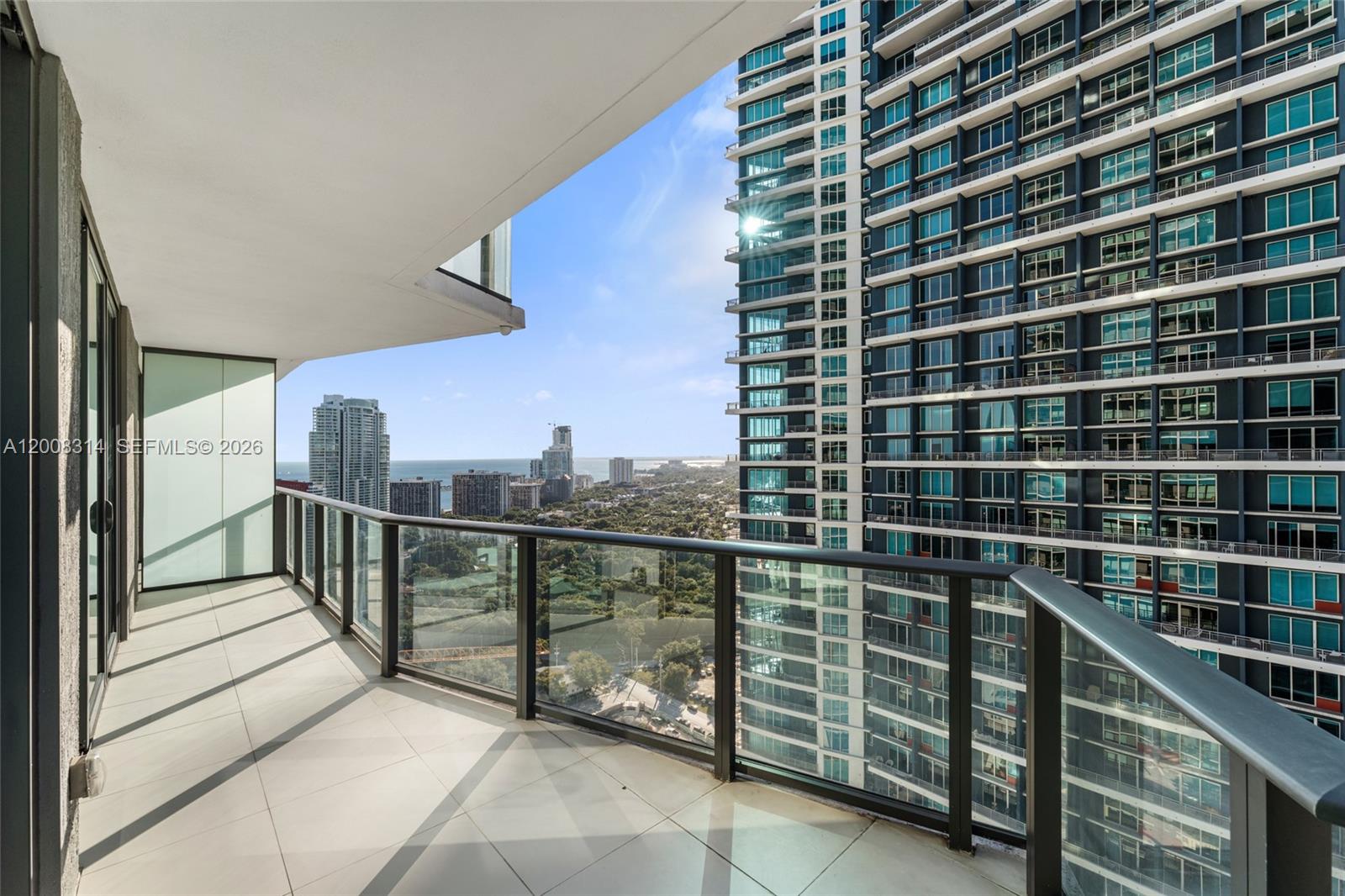 A high-rise balcony with glass railings overlooks a city skyline and the ocean — 1300 S Miami Ave # 2907, Miami FL 33130, MIAMI, FL