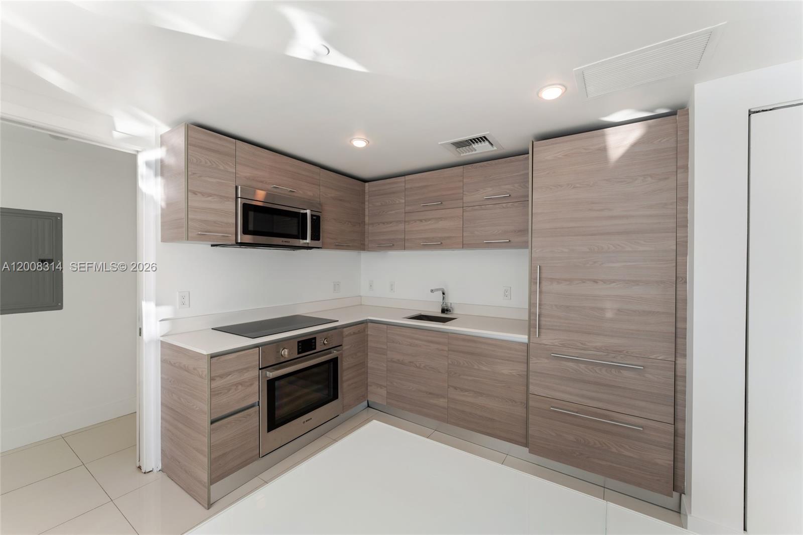 A modern kitchen features light wood-grain cabinetry, stainless steel appliances, and white countertops — 1300 S Miami Ave # 2907, Miami FL 33130, MIAMI, FL
