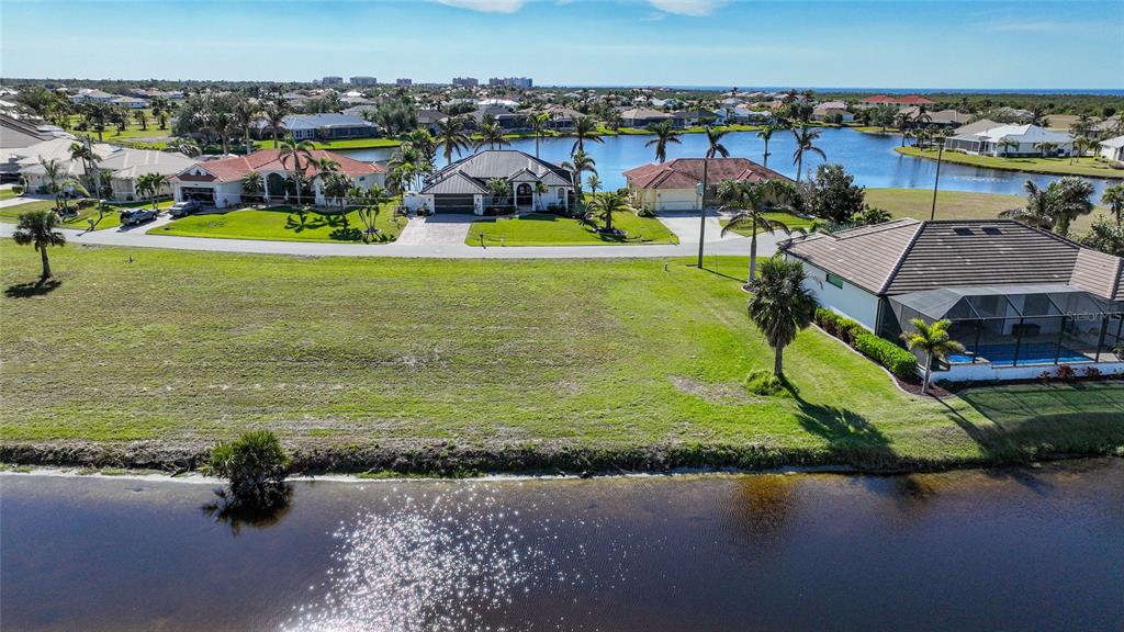 An aerial view shows a vacant grassy lot situated between two houses near a lake — 17146 ANTHEM LANE, PUNTA GORDA, FL