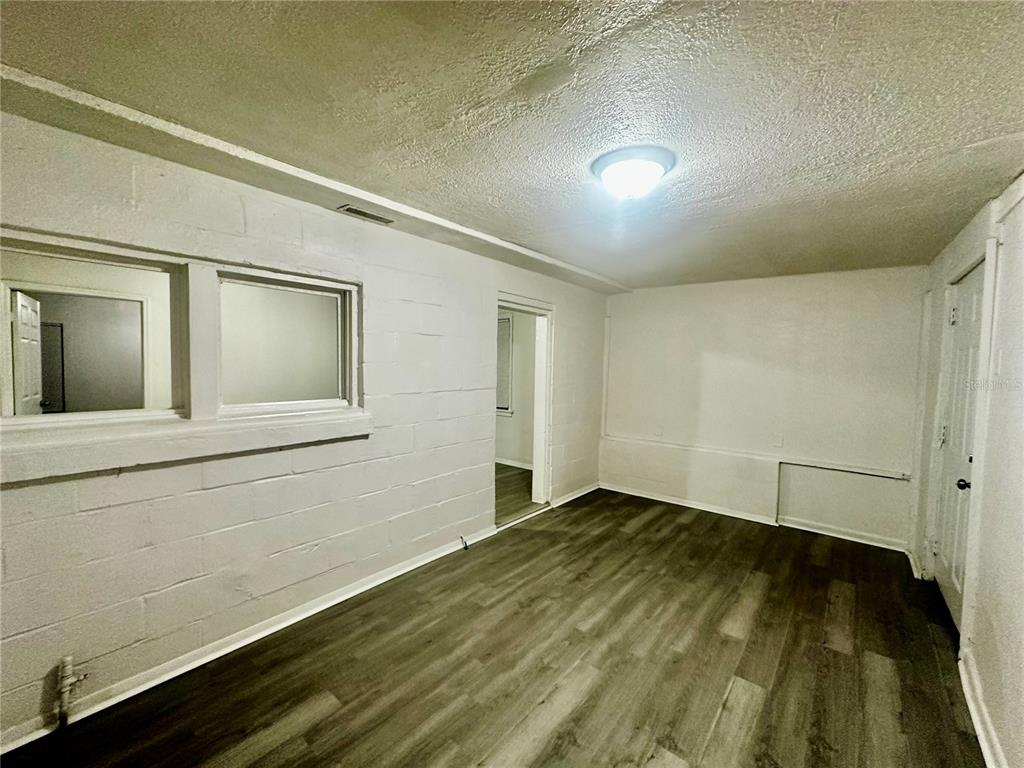 A room with white painted block walls, wood-look flooring, and a doorway leading to another room — 1907 S RIO GRANDE AVENUE, ORLANDO, FL