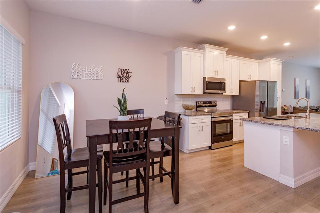 A kitchen and dining area with white cabinets, stainless steel appliances, and wood-look flooring — 884 KLONDIKE STREET, WINTER GARDEN, FL
