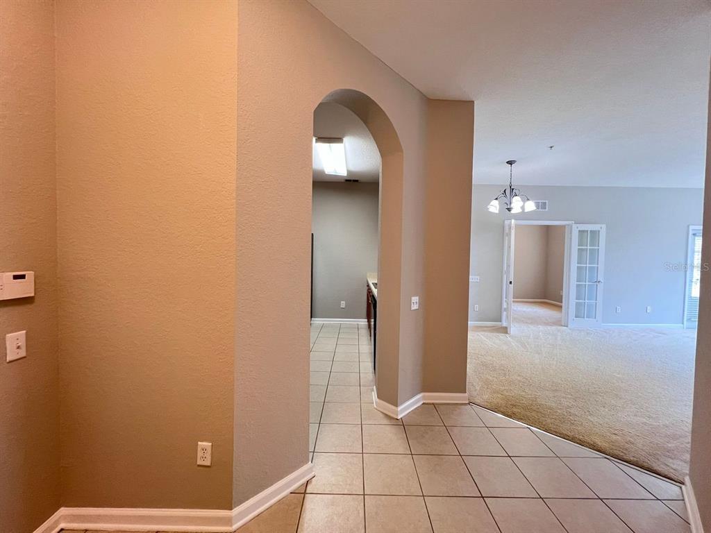 An arched doorway leads from a tiled entryway into a kitchen and carpeted living area — 2484 SAN TECLA STREET UNIT 204, ORLANDO, FL