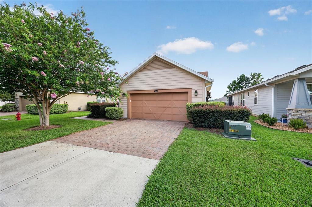 A tan house with a two-car garage, a brick driveway, and a blooming tree — 4845 NW 35TH LANE ROAD, OCALA, FL