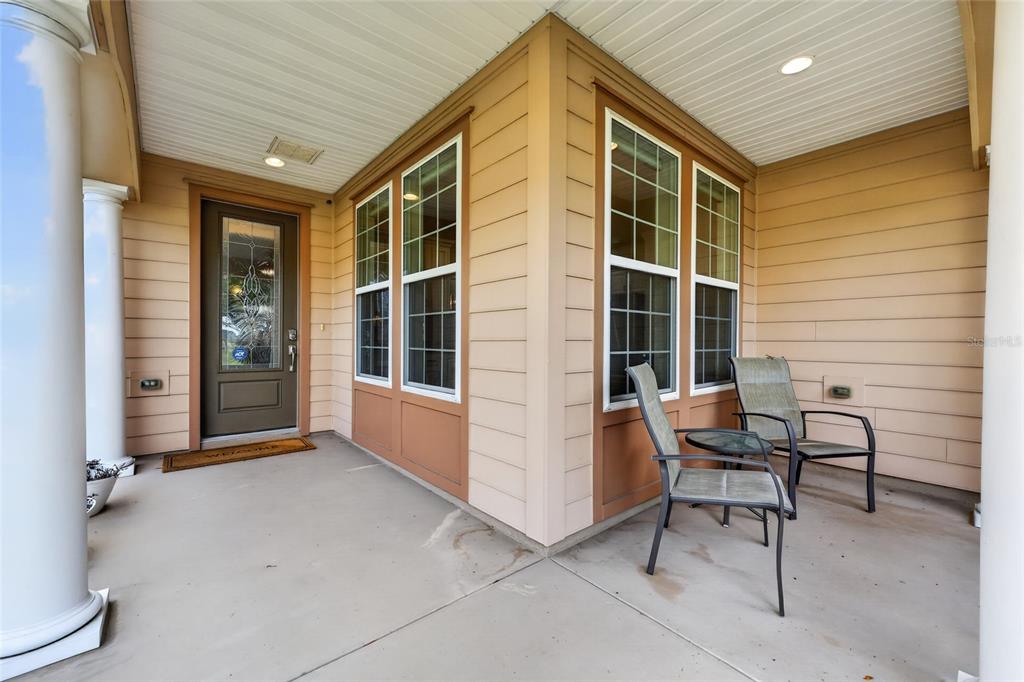 A covered front porch features tan siding, a glass-paneled door, and two chairs with a table — 4845 NW 35TH LANE ROAD, OCALA, FL