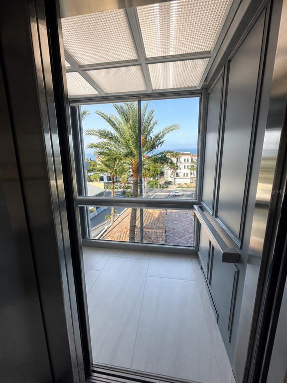 An elevator interior with a large glass window overlooking a palm tree and street — 3800 GULF BOULEVARD UNIT PH, ST PETERSBURG, FL