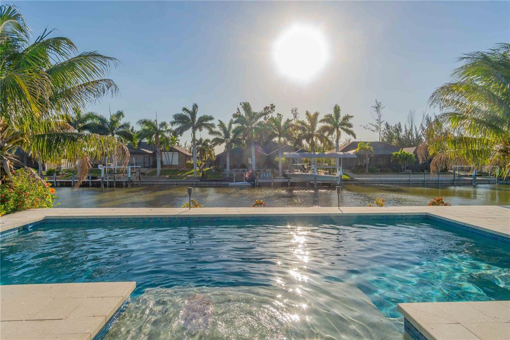 A swimming pool overlooks a canal lined with palm trees and residential homes — 8084 BURWELL CIRCLE, PORT CHARLOTTE, FL