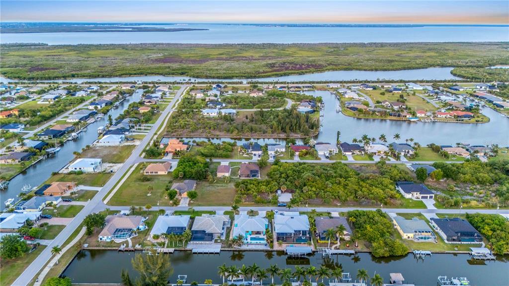 An aerial view shows a residential neighborhood with houses along canals leading to a bay — 8084 BURWELL CIRCLE, PORT CHARLOTTE, FL