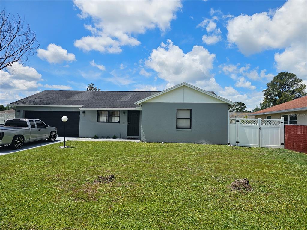 A single-story gray house with a black garage door and a white vinyl fence — 724 DEL RAY DRIVE, KISSIMMEE, FL