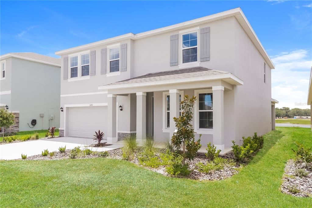 A two-story, light-gray stucco house features a front porch, a garage, and landscaped yard — 10832 CHARLOTTE DRIVE, PARRISH, FL