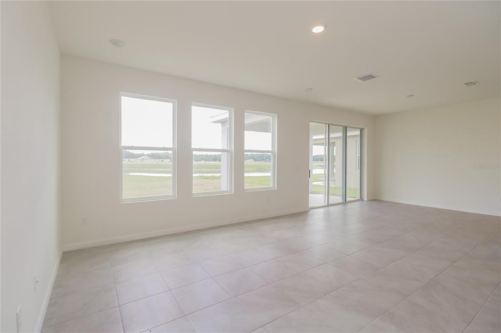 An empty living room features light-colored tile flooring, white walls, and large windows with views — 10832 CHARLOTTE DRIVE, PARRISH, FL