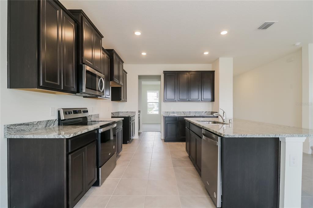 A kitchen features dark wood cabinets, granite countertops, stainless steel appliances, and tile flooring — 10832 CHARLOTTE DRIVE, PARRISH, FL