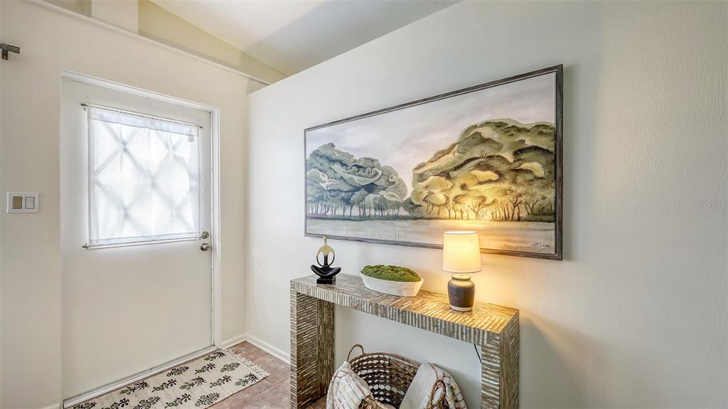 An entryway features a white door, a textured console table, and a landscape painting — 2551 WANETA DRIVE, SARASOTA, FL