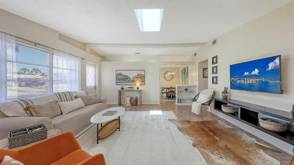 A living room features a beige sofa, a cowhide rug, a skylight, and a wall-mounted television — 2551 WANETA DRIVE, SARASOTA, FL