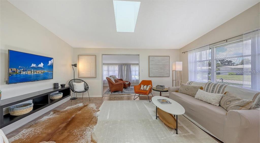 A living room features a television, a light-colored sofa, a cowhide rug, and a skylight — 2551 WANETA DRIVE, SARASOTA, FL