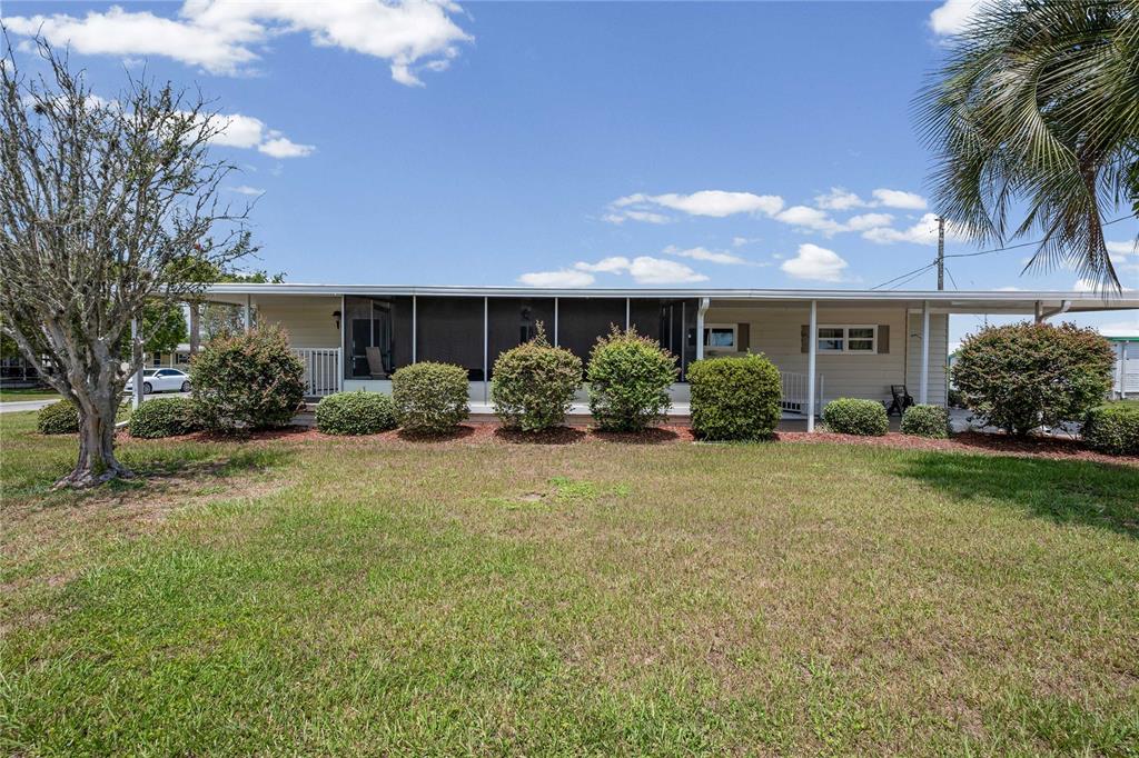 A single-story manufactured home with a screened-in porch and a carport under a blue sky — 36957 GRACE AVENUE, ZEPHYRHILLS, FL