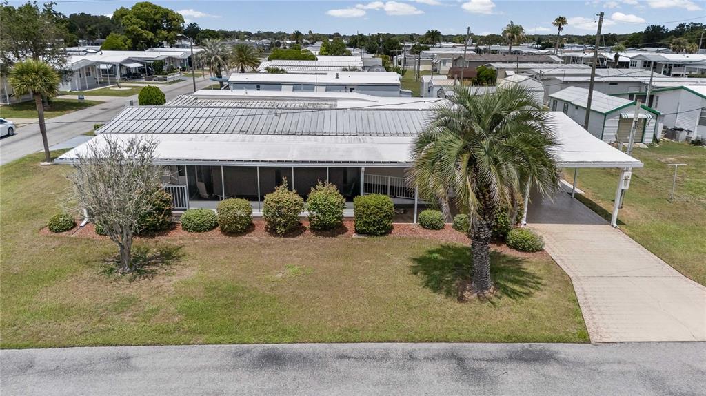 An elevated view of a single-story mobile home with a screened porch and carport — 36957 GRACE AVENUE, ZEPHYRHILLS, FL