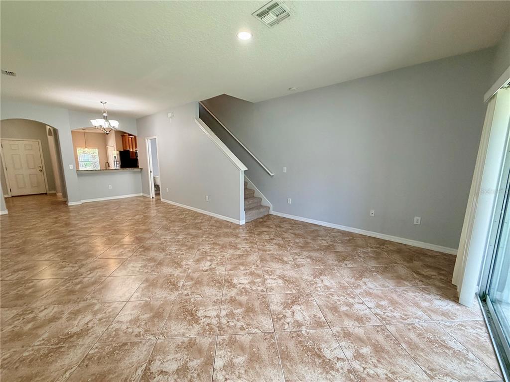 An open living area features tile flooring, a staircase, and a view into the kitchen — 31150 GOSSAMER WAY, WESLEY CHAPEL, FL