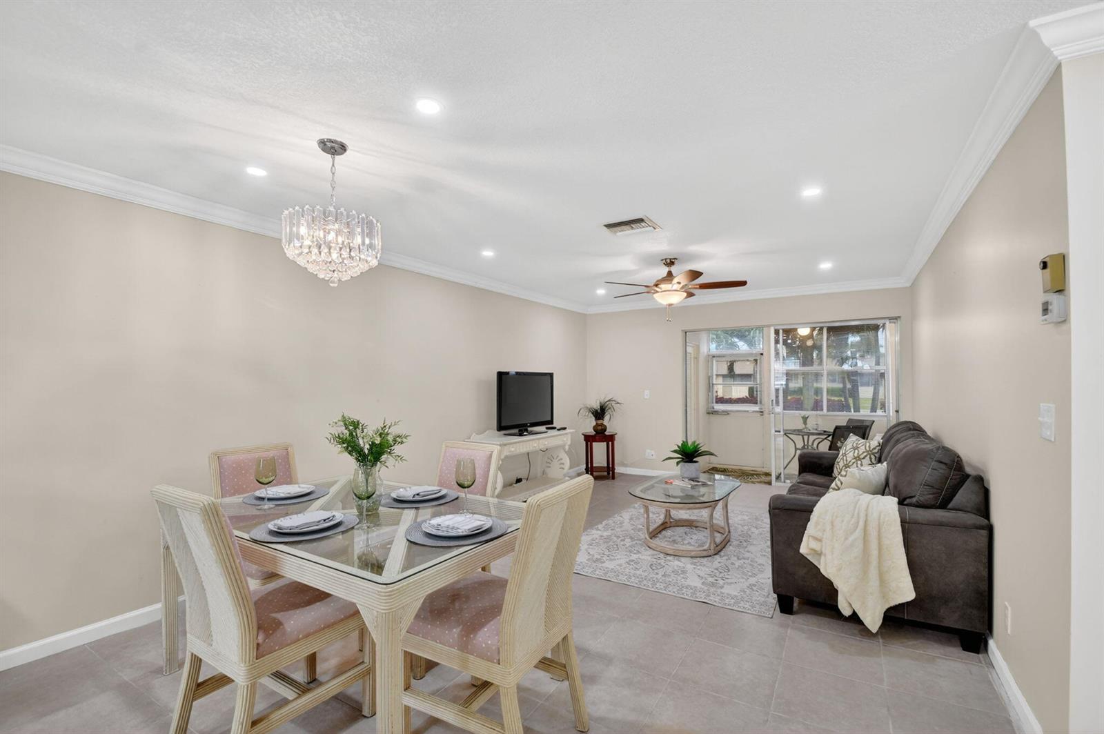 A dining area with a glass table and chandelier opens into a living room with tile — 2787 Dudley Dr Apt D, West Palm Beach FL 33415, WEST PALM BEACH, FL