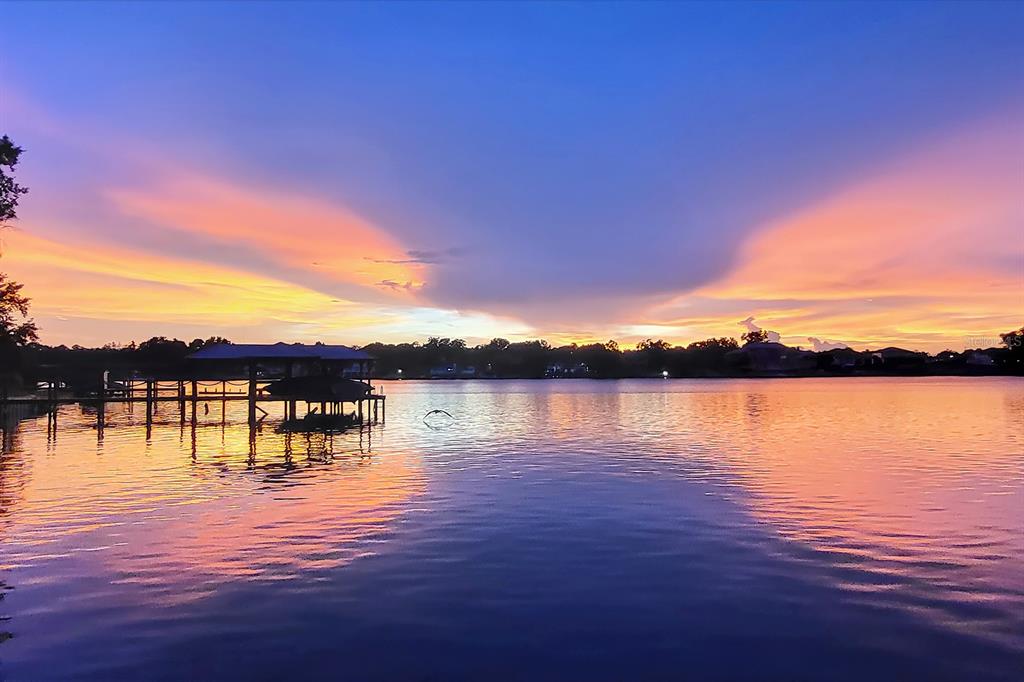 A wooden boat dock extends into a calm lake under a vibrant sunset sky — 1351 N CLASSIC COURT, LONGWOOD, FL