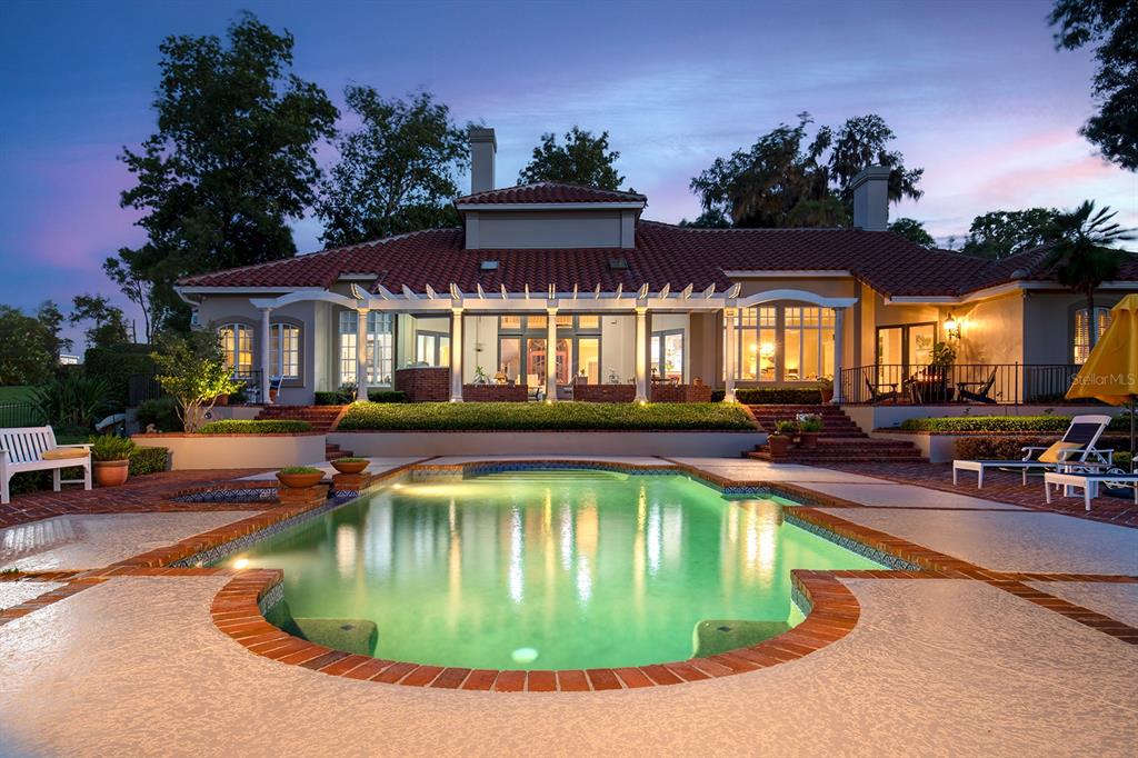 A backyard swimming pool sits in front of a house with a tiled roof and pergola — 1351 N CLASSIC COURT, LONGWOOD, FL