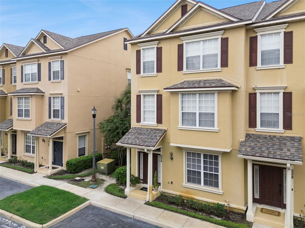 An exterior view of two adjacent three-story tan townhomes with brown shutters and shingled roofs — 624 PENSACOLA LANE, LAKE MARY, FL