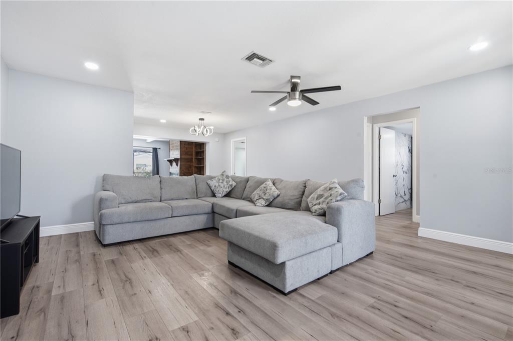 A living room features light gray walls, wood-look flooring, and a large gray sectional sofa — 1811 FOREST DRIVE, OLDSMAR, FL