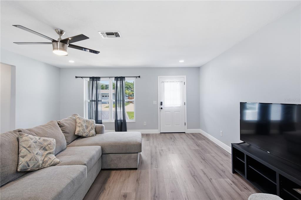 A living room features light gray walls, wood-look flooring, a sectional sofa, and a ceiling fan — 1811 FOREST DRIVE, OLDSMAR, FL