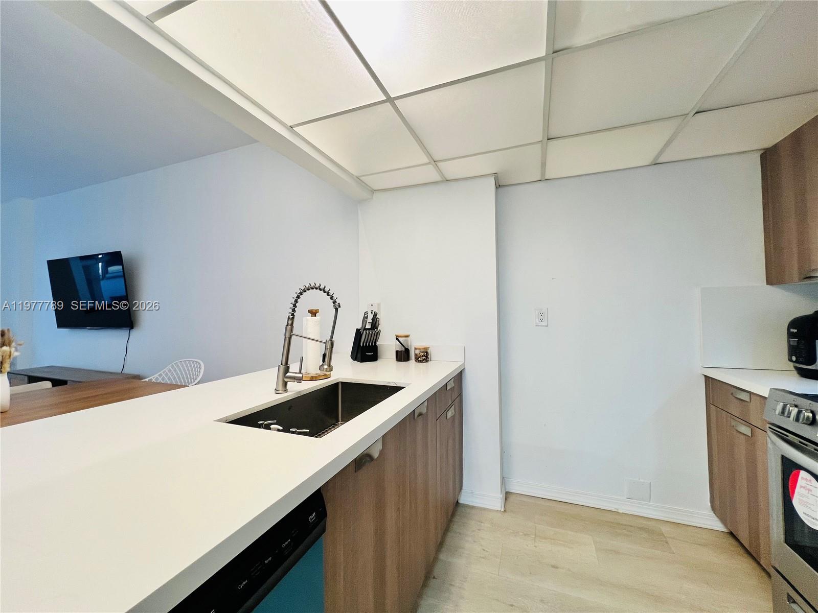 A kitchen features a white countertop, wood-toned cabinets, a stainless steel sink, and a drop ceiling — 540 Brickell Key Dr # 202, Miami FL 33131, MIAMI, FL
