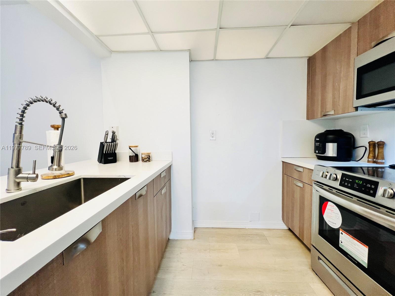 A galley kitchen features wood-tone cabinets, white countertops, stainless steel appliances, and a drop ceiling — 540 Brickell Key Dr # 202, Miami FL 33131, MIAMI, FL