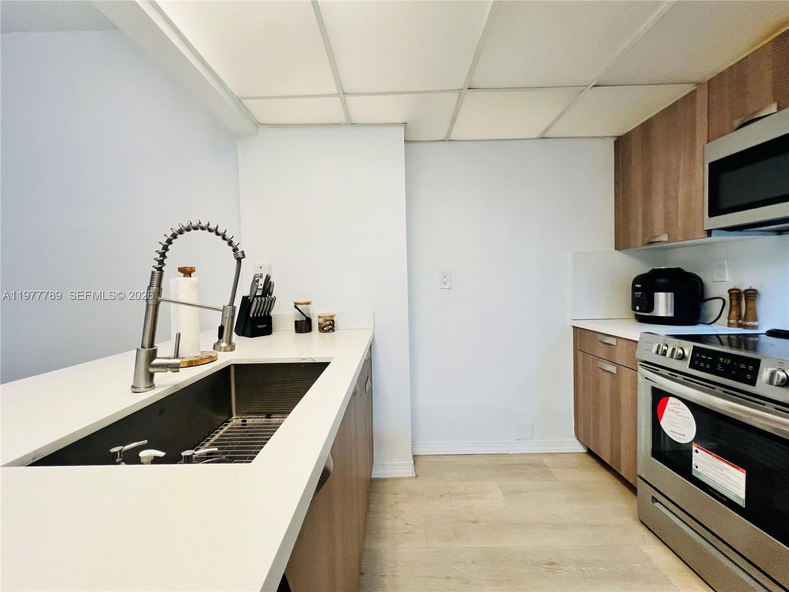 A modern kitchen features light wood cabinets, white countertops, a stainless steel sink, and appliances — 540 Brickell Key Dr # 202, Miami FL 33131, MIAMI, FL