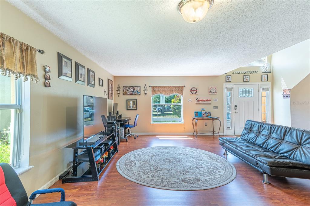 A living room with wood-look flooring, a black futon, a desk, and a round rug — 407 SAMUEL STREET, DAVENPORT, FL