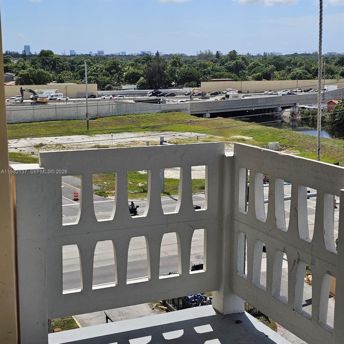 A balcony with a decorative concrete railing overlooks a highway, construction site, and distant cityscape — 15600 NW 7th Ave # 703, Miami FL 33169, MIAMI, FL