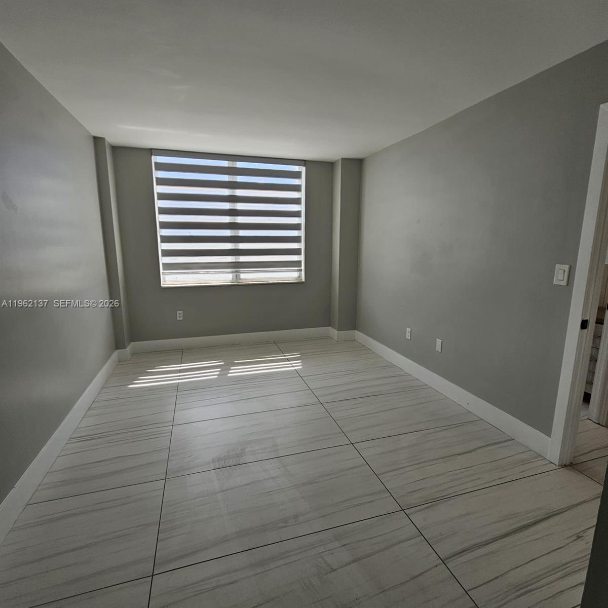 An empty room features light gray walls, white baseboards, and large, light-colored tiled flooring — 15600 NW 7th Ave # 703, Miami FL 33169, MIAMI, FL
