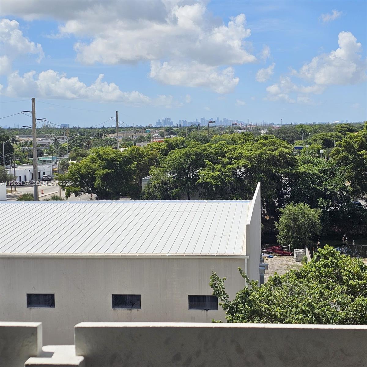 An elevated view shows a metal-roofed building, surrounding trees, and a distant city skyline — 15600 NW 7th Ave # 703, Miami FL 33169, MIAMI, FL
