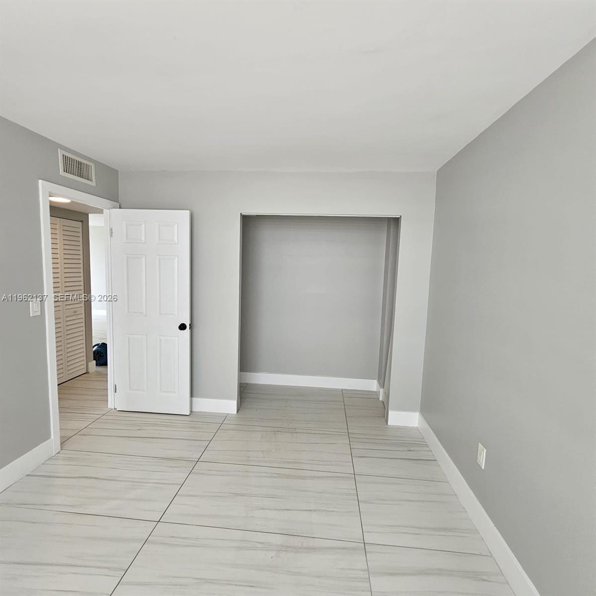 A room with light gray walls, large light-colored floor tiles, and an open closet space — 15600 NW 7th Ave # 703, Miami FL 33169, MIAMI, FL