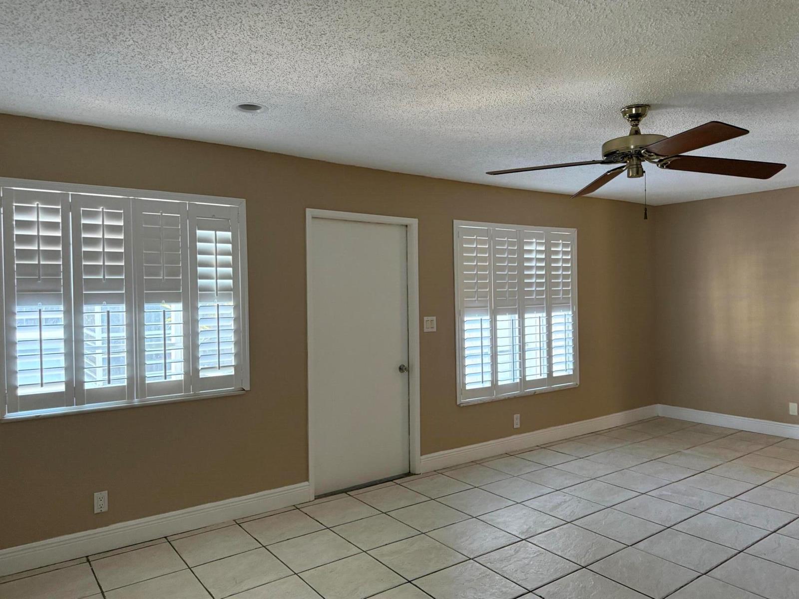 A room with beige walls, white plantation shutters, a ceiling fan, and light-colored tile flooring — 320 SE 10th Street # C, Pompano Beach FL 33060, POMPANO BEACH, FL