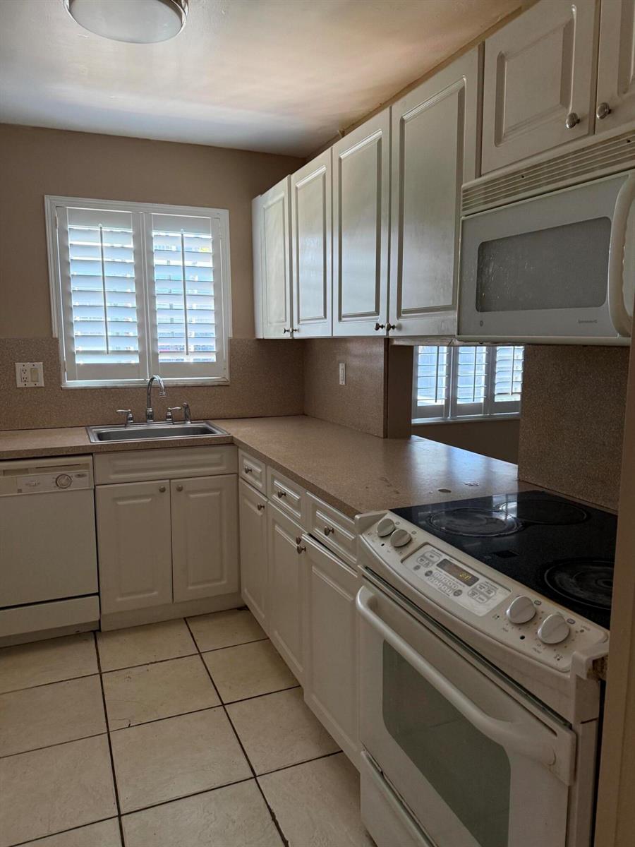 A kitchen features white cabinetry, a white stove, a dishwasher, and a window with shutters — 320 SE 10th Street # C, Pompano Beach FL 33060, POMPANO BEACH, FL