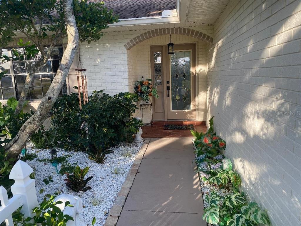 A concrete walkway leads to the front entrance of a house with white brick walls — 8437 GIBRALTER STREET, SPRING HILL, FL