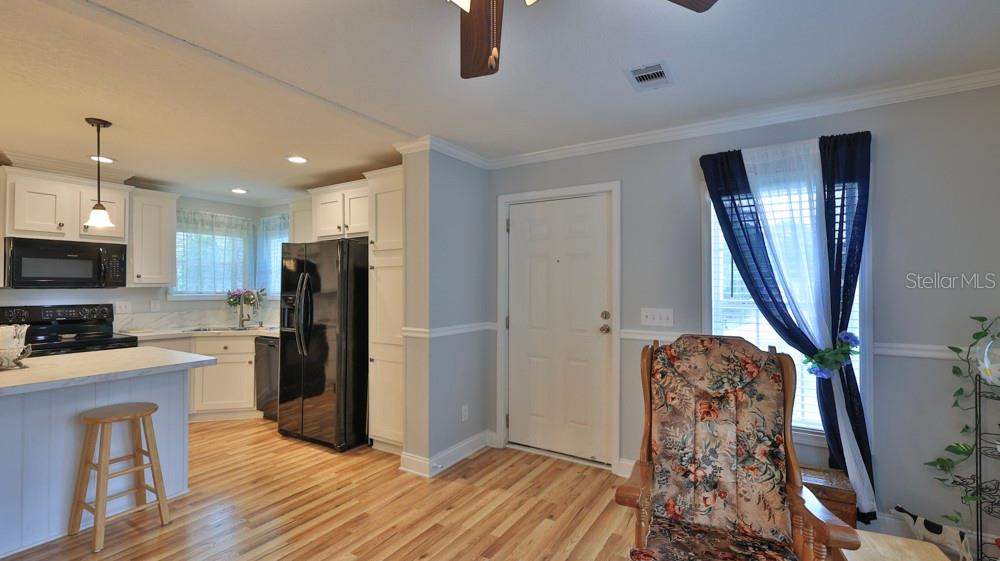 A kitchen with white cabinets and black appliances opens into a room with a rocking chair — 1157 MILLBROOK AVENUE, PORT ORANGE, FL