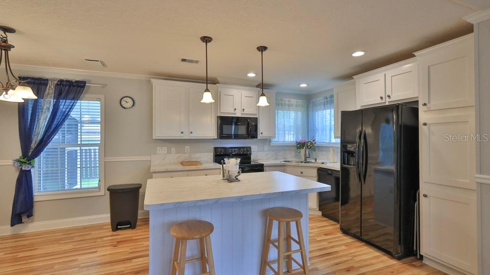 A kitchen features white cabinets, a marble-topped island, black appliances, and light wood flooring — 1157 MILLBROOK AVENUE, PORT ORANGE, FL