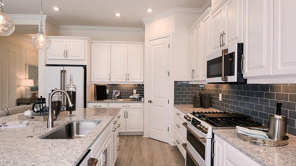 A kitchen features white cabinets, a granite island with bar seating, and a gray backsplash — 3208 VICENZA COURT, BRADENTON, FL