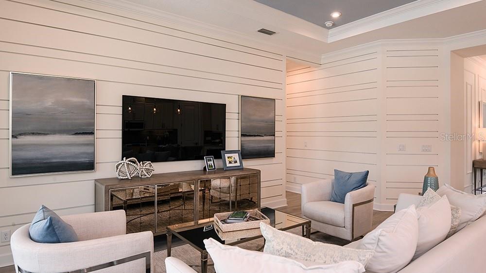 An open-concept living room and kitchen feature white cabinetry, shiplap walls, and neutral furnishings — 3208 VICENZA COURT, BRADENTON, FL