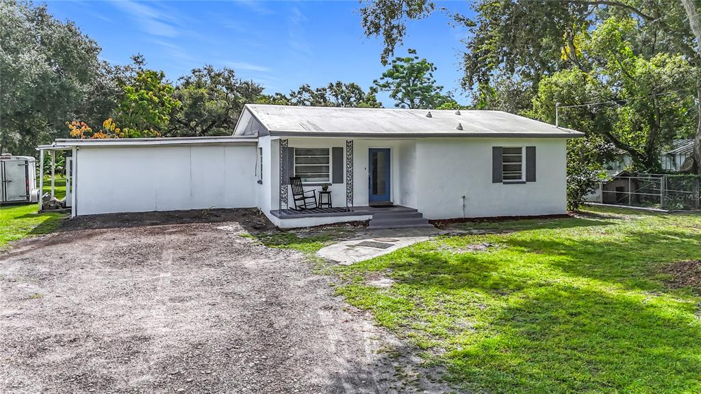 A single-story white house with a metal roof, front porch, and gravel driveway — 8016 FORMBY STREET, RIVERVIEW, FL