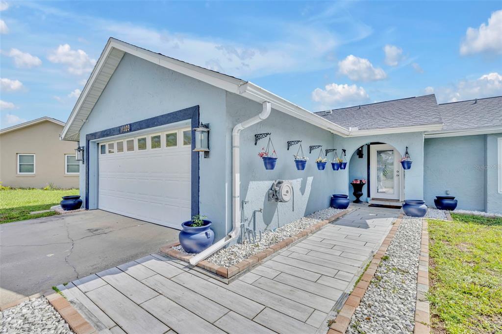 A light blue house exterior features a garage, a paved walkway, and hanging blue planters — 11103 ARIES DRIVE, ORLANDO, FL