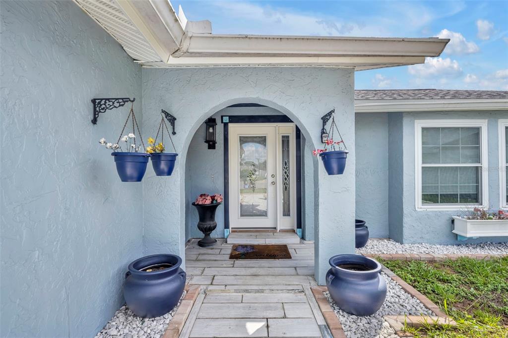 A light blue house exterior features an arched entryway with a white door and planters — 11103 ARIES DRIVE, ORLANDO, FL