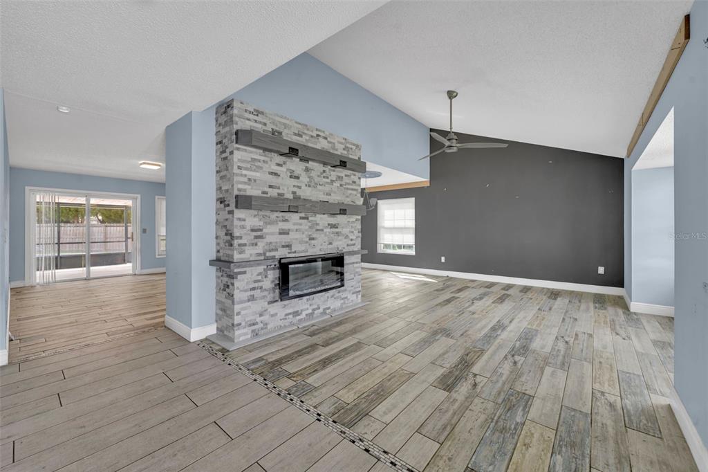 A living room features a stone fireplace, wood-look tile flooring, and a vaulted ceiling — 11103 ARIES DRIVE, ORLANDO, FL