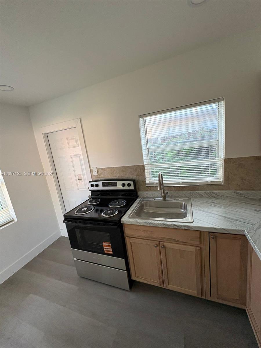 A kitchen features light wood cabinets, a marble-patterned countertop, a stainless steel stove, and a window — 2316 Madison St # 6, Hollywood FL 33020, HOLLYWOOD, FL