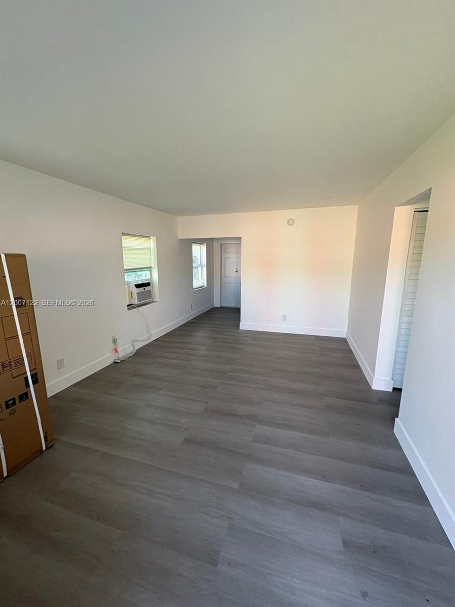 An empty room features gray wood-look flooring, white walls, and a window air conditioning unit — 2316 Madison St # 6, Hollywood FL 33020, HOLLYWOOD, FL