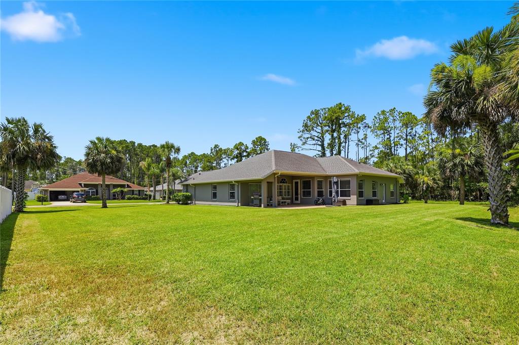 A wide view of a single-story house exterior with a large green lawn and palm trees — 62 SENTINEL TRAIL, PALM COAST, FL